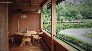 Ein Holzinterieur mit einem runden Tisch und Stühlen, einer Hängeleuchte und Blick auf eine grüne Landschaft mit einer Straße und Gebäuden.