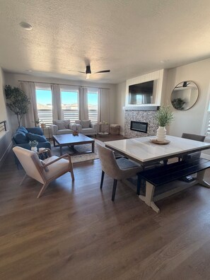 A modern living room with a dining area, a fireplace, and a large window. - 4-bedroom new house in adorable Cedar City with furnished basement (Cedar City)
