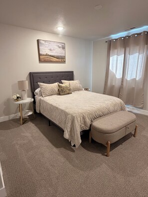 A bedroom with a bed, bedside table, lamp, and curtains. - 4-bedroom new house in adorable Cedar City with furnished basement (Cedar City)