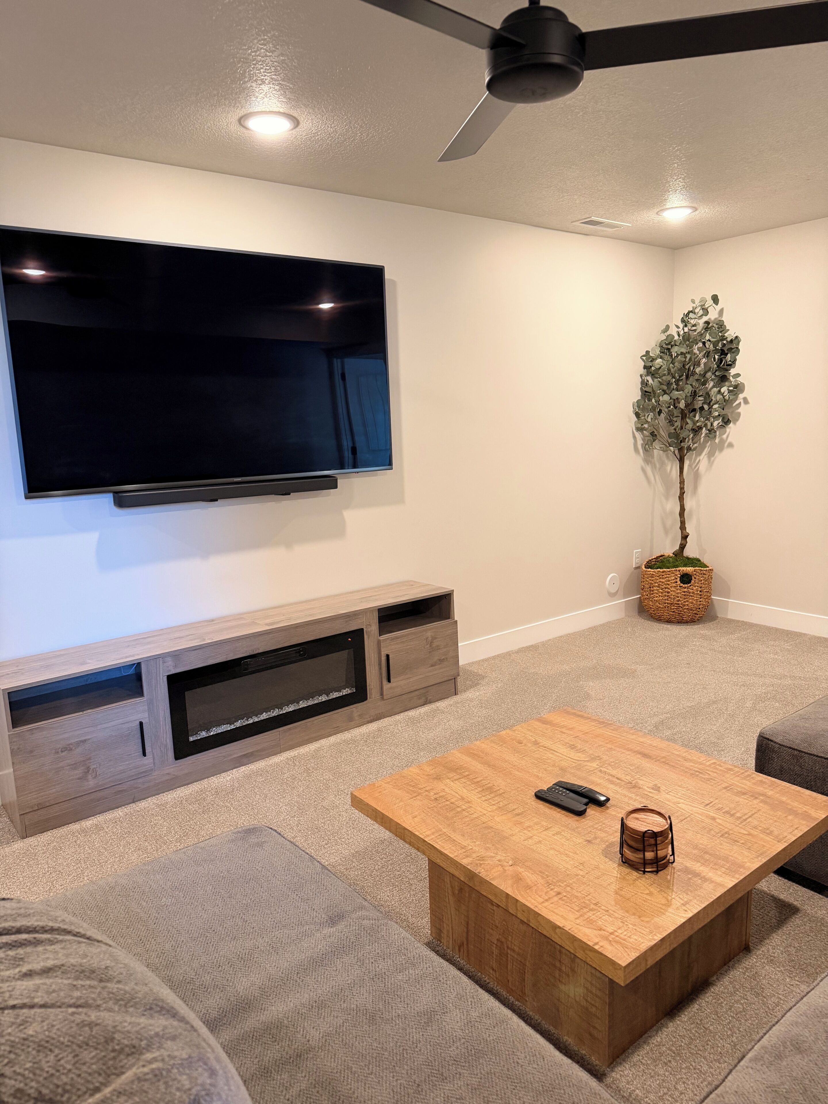 A modern living room with a flat-screen TV, wooden entertainment unit, a coffee table, and a ceiling fan.