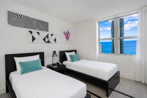 Habitación de hotel con dos camas, una mesita de noche con lámpara y una obra de arte en la pared.