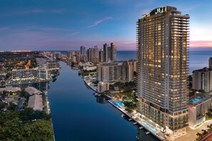 A high-rise hotel with a pool on the ground floor, surrounded by a marina and other buildings.