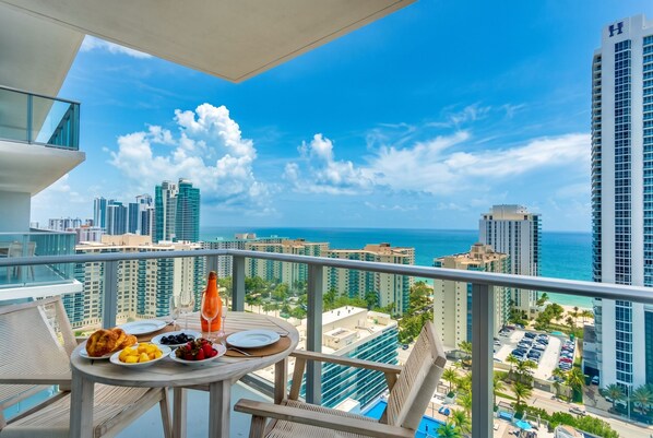 A balcony with a table set for breakfast, overlooking a cityscape and the ocean.