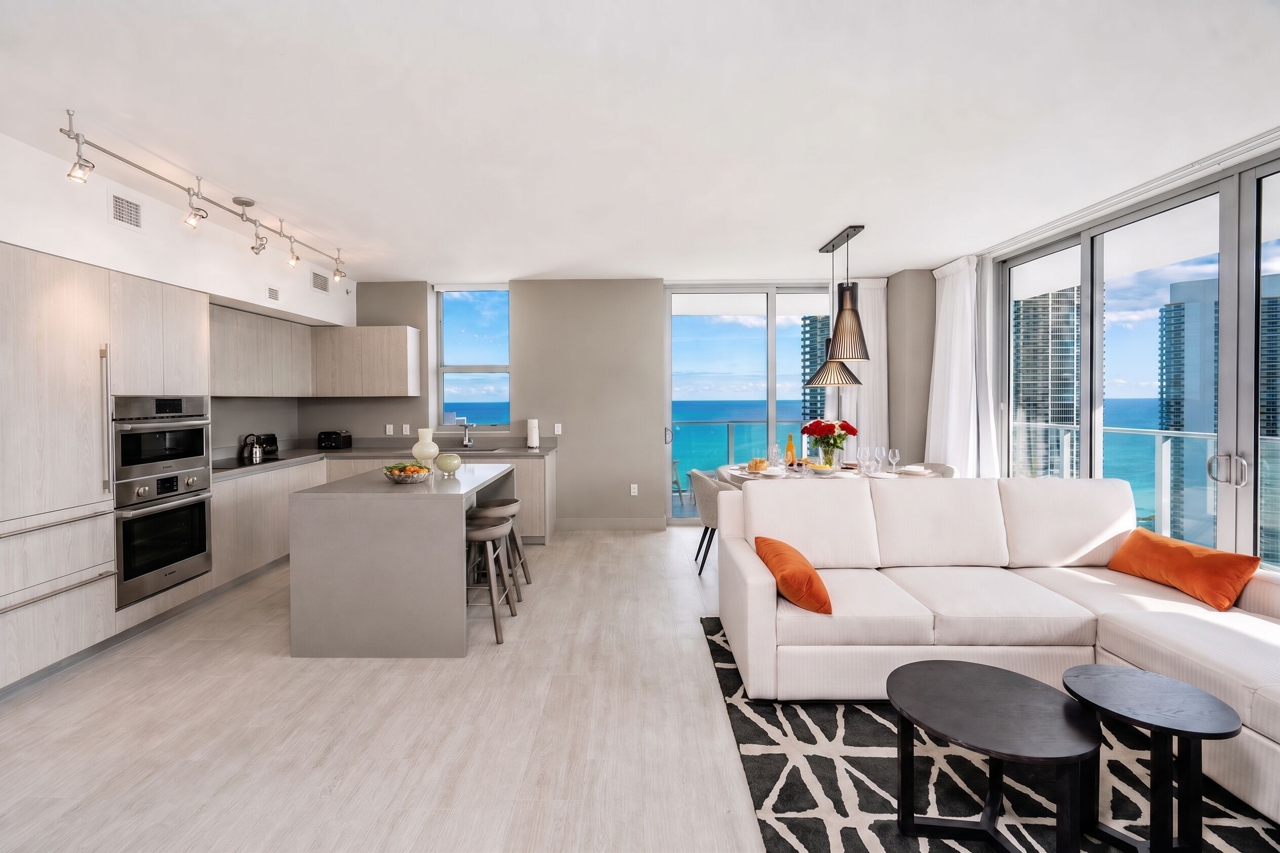 A modern apartment with a kitchen, dining area, and living room, featuring a large window with a city view.