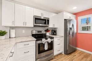 A kitchen with white cabinets, stainless steel appliances, and a wooden floor. - BEACHFRONT SUNSETS TO DIE FOR (Madeira Beach)