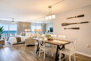 Hotelkamer met een bed, een eettafel, stoelen, een televisie en een balkon met uitzicht op zee.