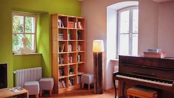 Ein Zimmer mit einem Klavier, einem Bücherregal, einer Lampe und einem Fenster.