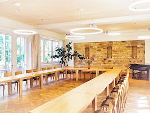 A spacious conference room with a long table, multiple chairs, a piano, and a stone wall.