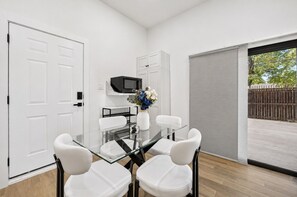 Ein moderner Essbereich mit einem Glastisch, weißen Stühlen und einer Vase mit Blumen.