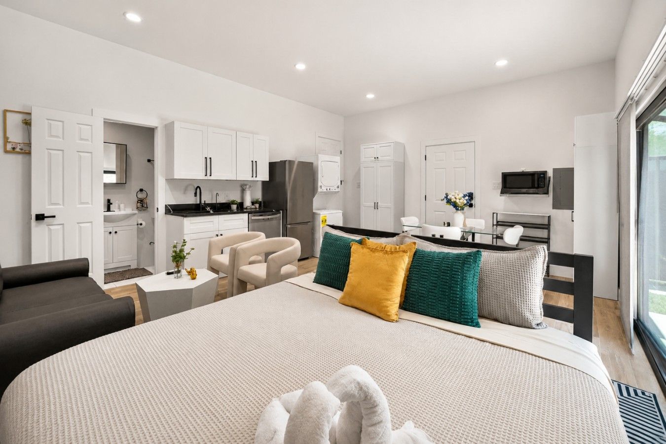 Une chambre d’hôtel moderne dotée d’un grand lit, d’un coin salon avec un canapé et des fauteuils, d’une kitchenette et d’un coin repas.