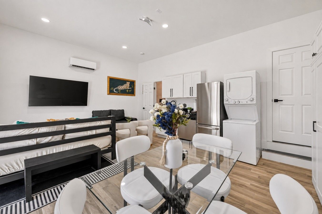 A modern living room with a sofa, a glass dining table, and a kitchen area with white cabinets and appliances.