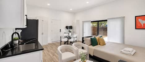 A modern apartment with a kitchenette, a dining area, a living room with a sofa and a TV, and a large window.