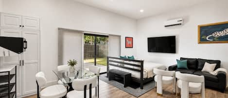 Uma sala de estar moderna com uma mesa de jantar de vidro, um sofá e uma televisão fixada na parede.