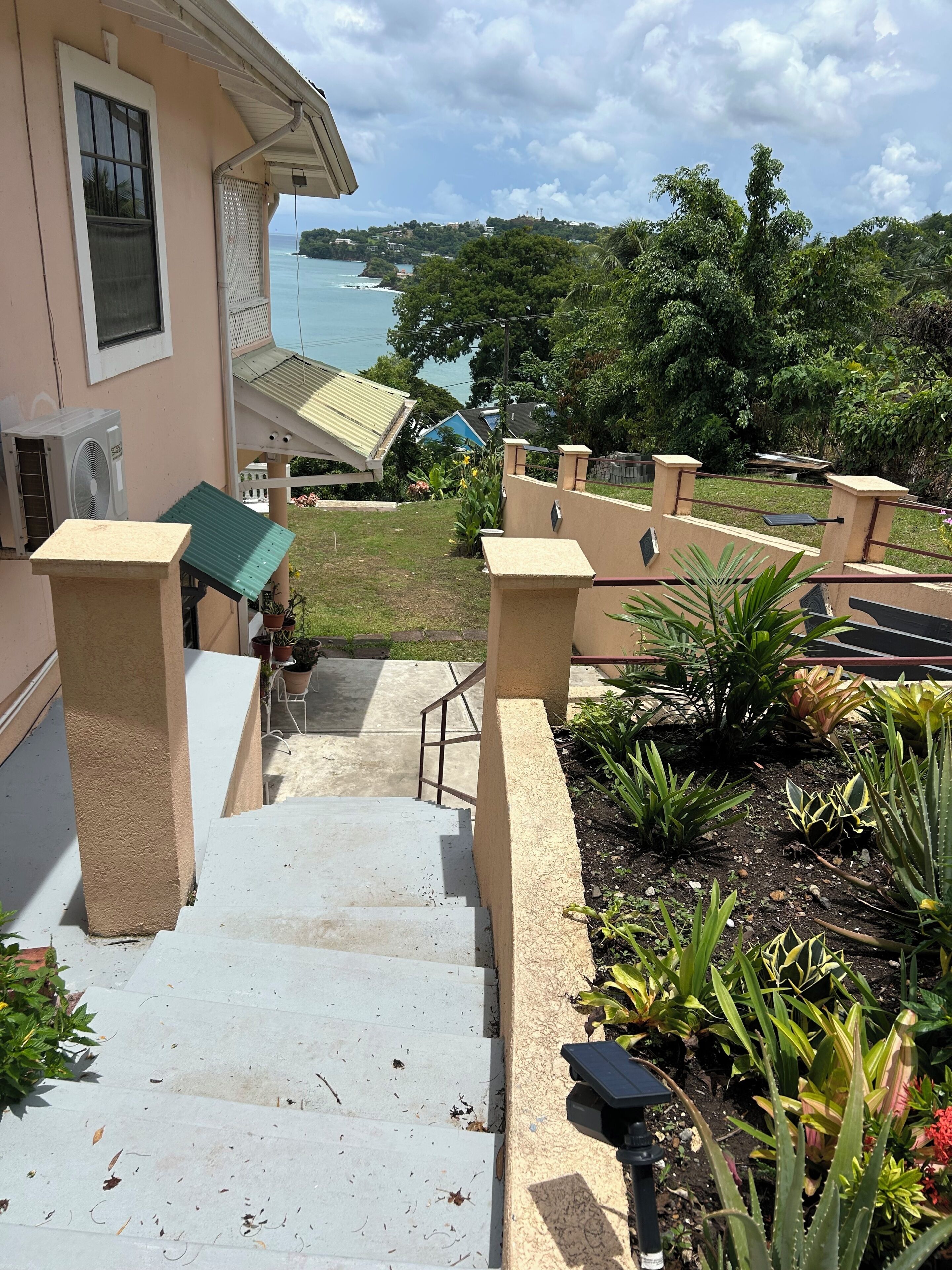 A staircase leading to a building with a view of the sea, surrounded by greenery and a small garden.