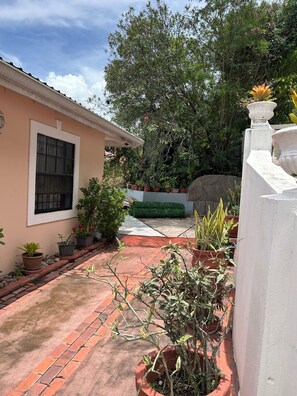 A courtyard with a building, potted plants, a stone pathway, and a large tree. - Belle Escape - Blue Room (Castries)