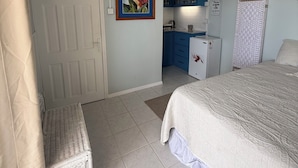 A bedroom with a bed, a bench, a kitchenette, and a door. - Belle Escape - Blue Room (Castries)