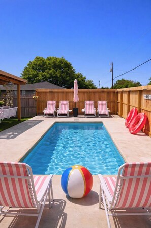 A rectangular swimming pool with six striped lounge chairs and a beach ball. - Pink•Heated Pool•Pro Karaoke System•Glam Getaway (Fredericksburg)
