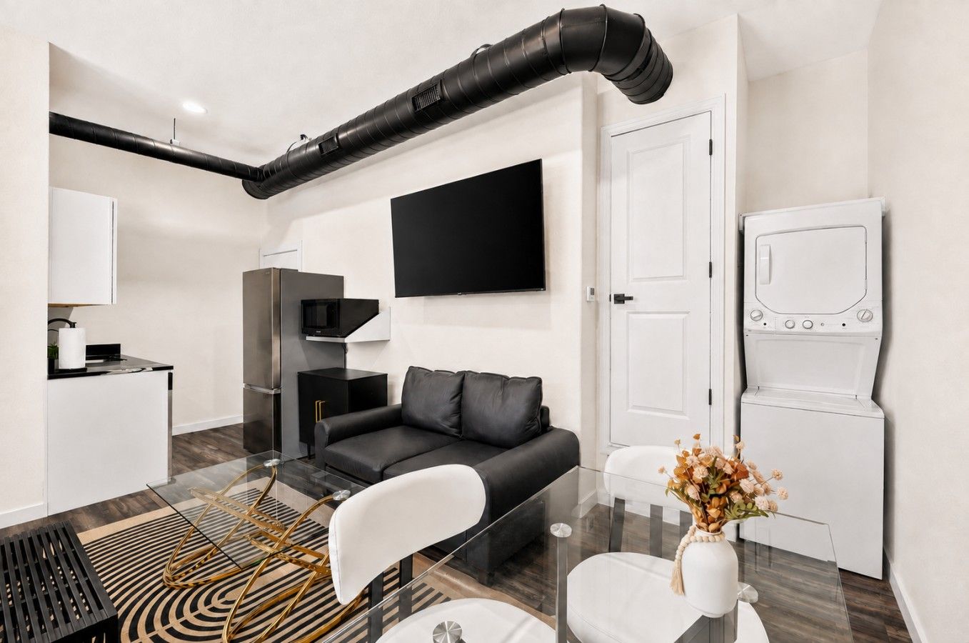 A modern living room with a black sofa, a glass coffee table, and a white door.