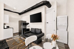 A modern living room with a black sofa, a glass coffee table, and a white door. - Settle into a modern, private upper-floor studio designed to make an extended Dallas stay feel easy and comfortable. (Dallas)