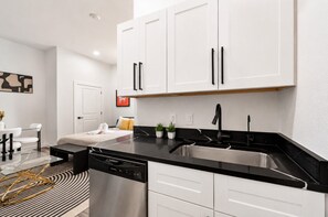 A modern kitchen with white cabinets, a black countertop, and stainless steel appliances. - Settle into a modern, private upper-floor studio designed to make an extended Dallas stay feel easy and comfortable. (Dallas)