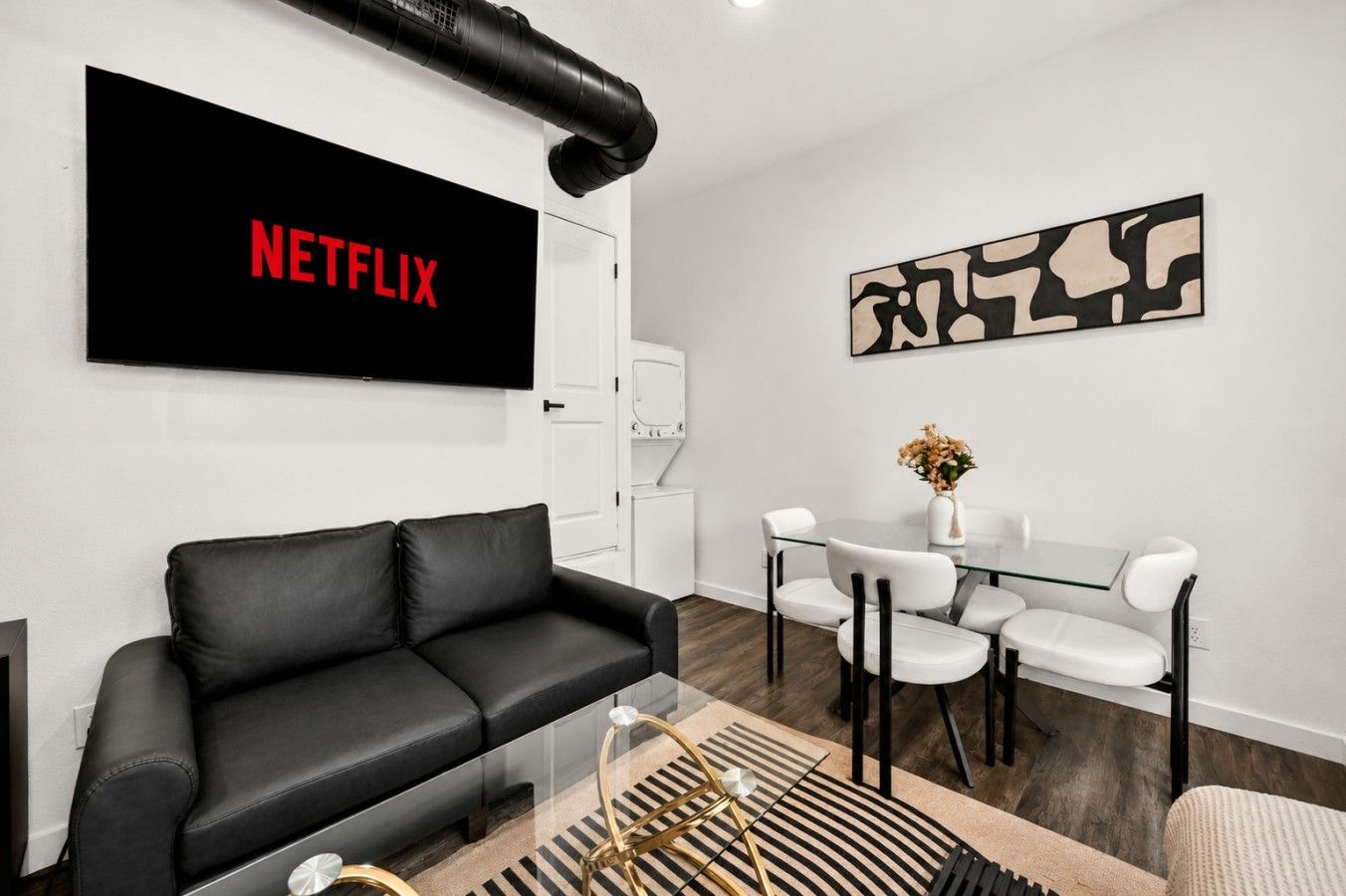 Una sala de estar moderna con un sofá de cuero negro, una mesa de centro de vidrio y un televisor de pantalla plana mostrando 'NETFLIX'.