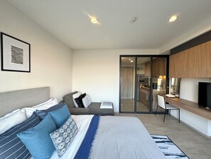 Ein modernes Schlafzimmer mit Bett, Nachttisch und Blick zur Küche.