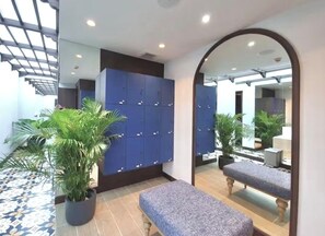 Een hotel lobby met een zithoek, een spiegel die de ruimte weerspiegelt, en een rij lockers.