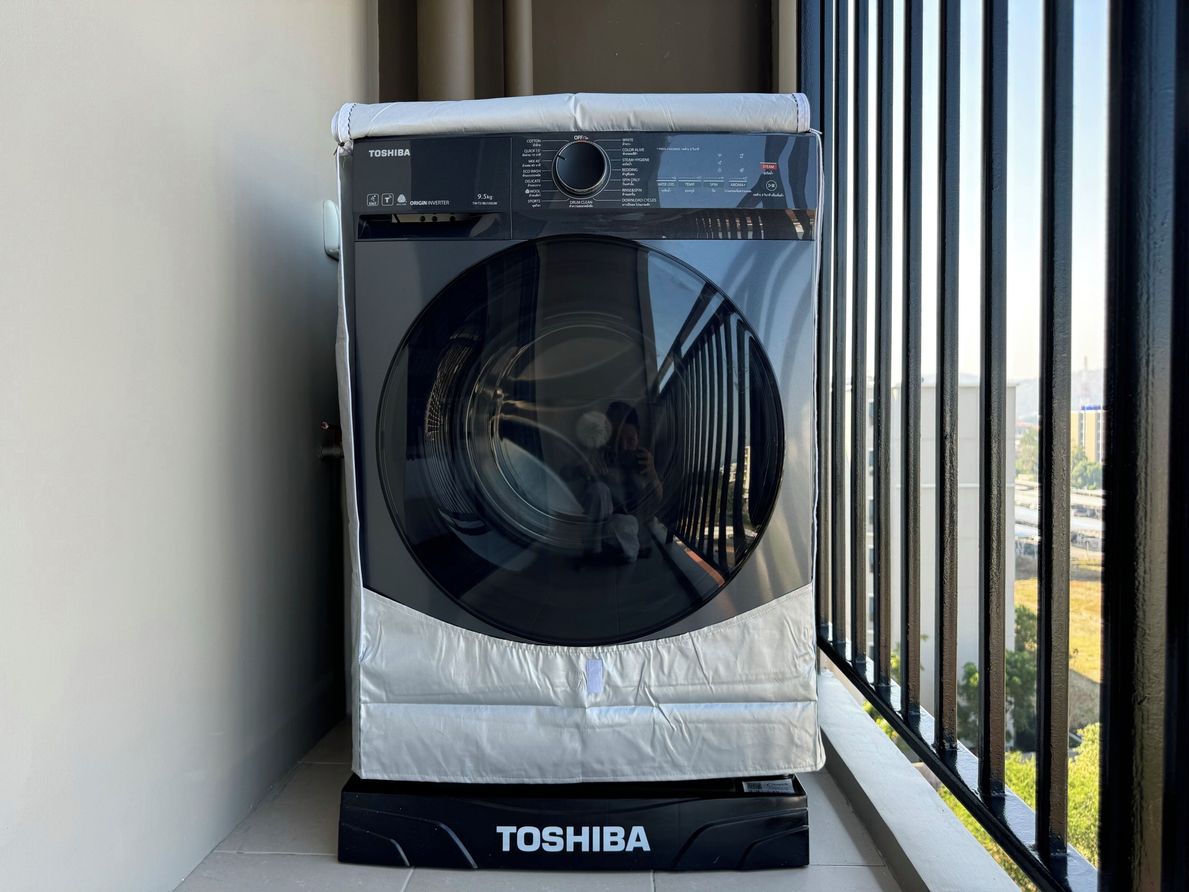 Una lavadora Toshiba negra en un rincón con vista al exterior.