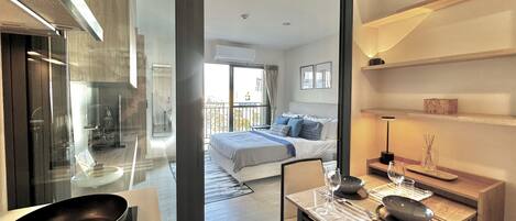 A modern hotel room with a large bed, a dining area with a table set for two, and a view of the balcony.