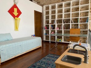 A compact room with a bed, a small table with a sink, a bookshelf, and a red traffic sign on the wall.