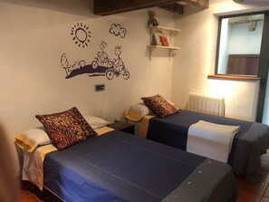 A room with two beds, a wall mural, a shelf with items, and a window.