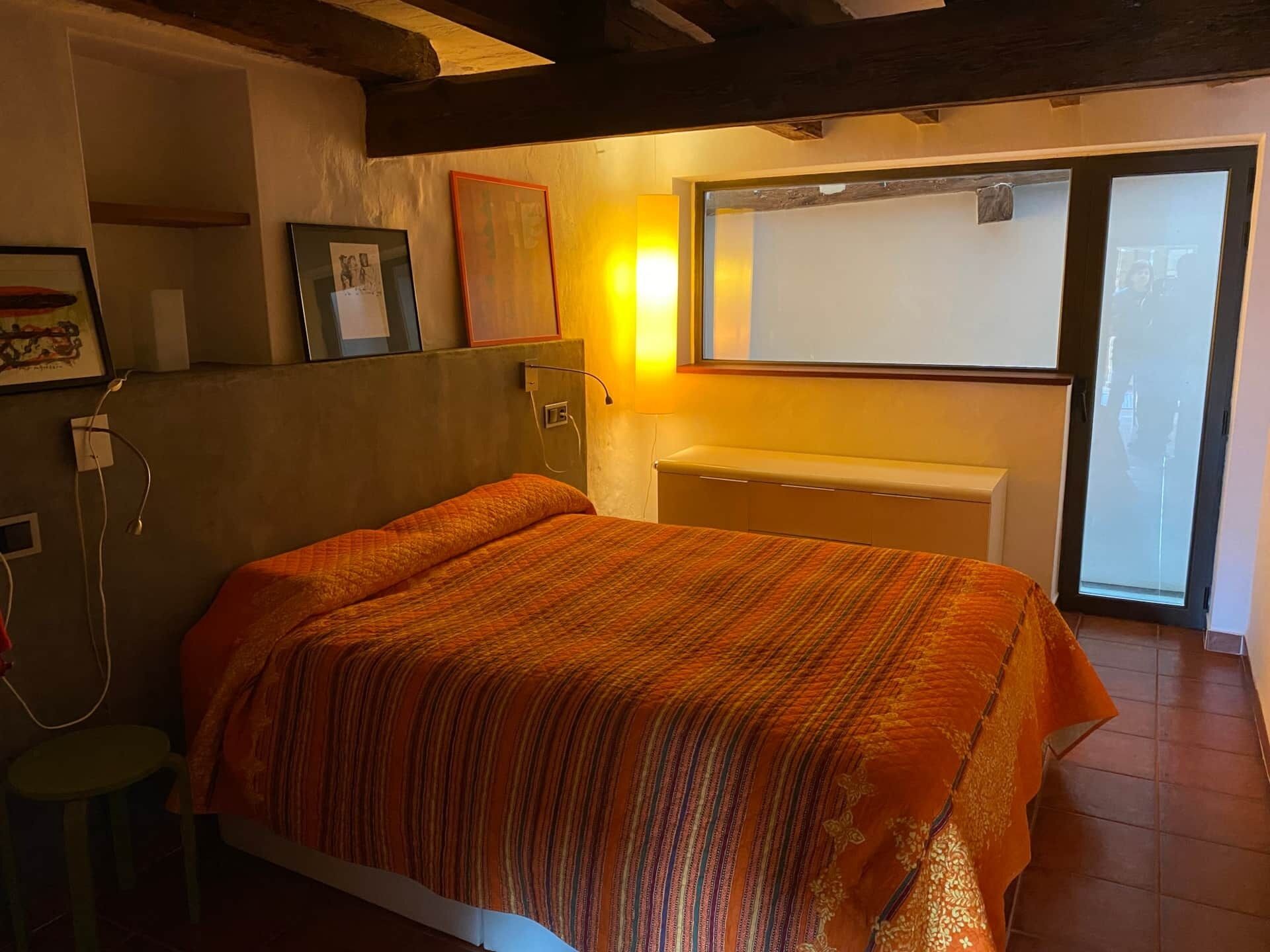 A bedroom with a bed, a wall-mounted lamp, and a window.