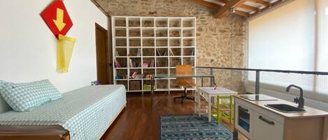 Une pièce de taille modeste comprenant un lit, une petite table, un coin cuisine et une bibliothèque.
