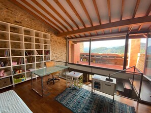 A room with a large window, a desk, a bookshelf, and a view of a mountainous landscape. - Stone Country House in La Tinença de Benifassà · Nature and a Fireplace (El Bellestar)