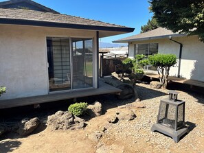 A modern house with a sliding glass door, a small garden with rocks and a tree, and a metal fire feature.