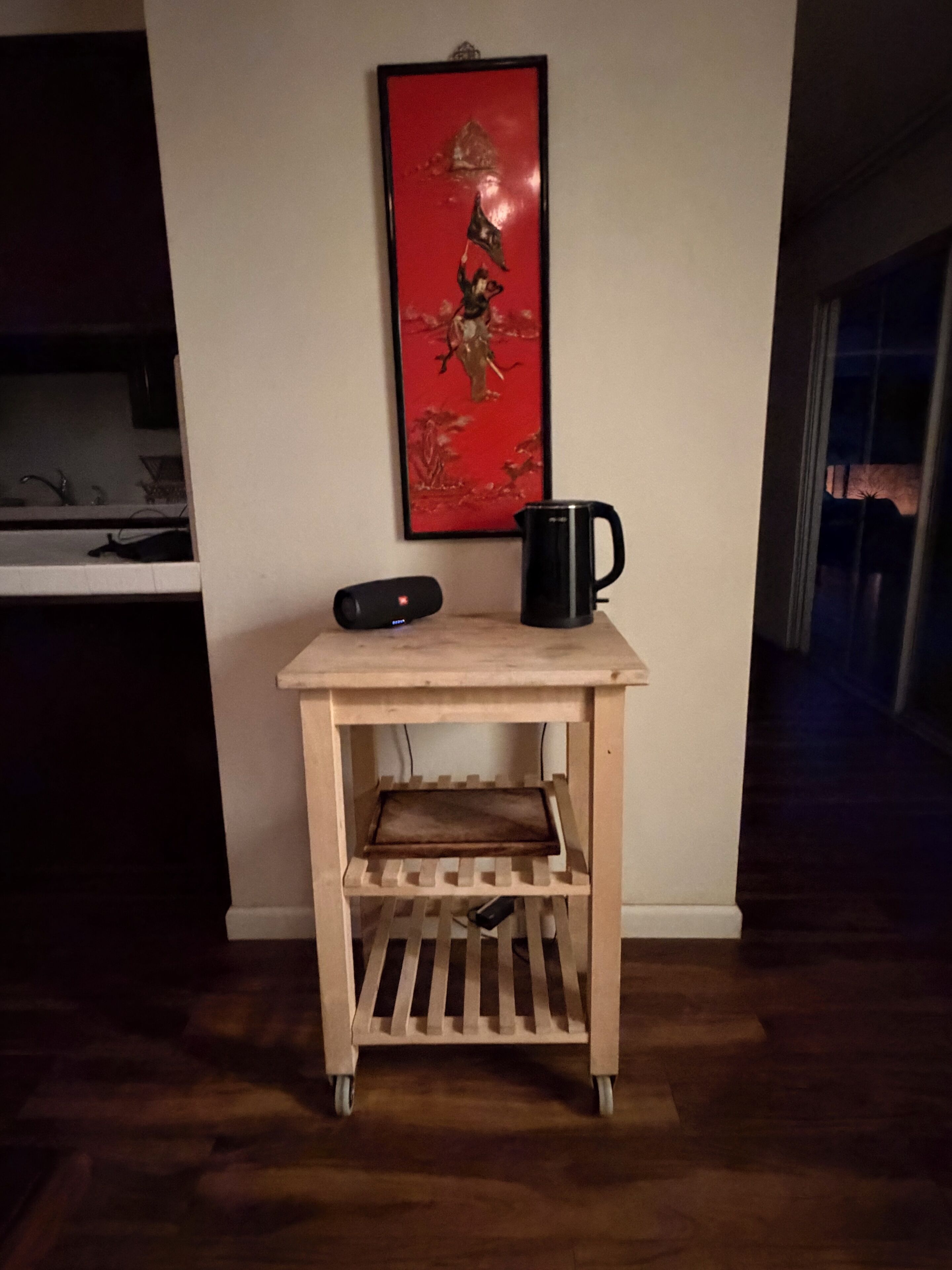 A small wooden table with a black mug and a speaker on it, placed against a wall with a framed picture above.