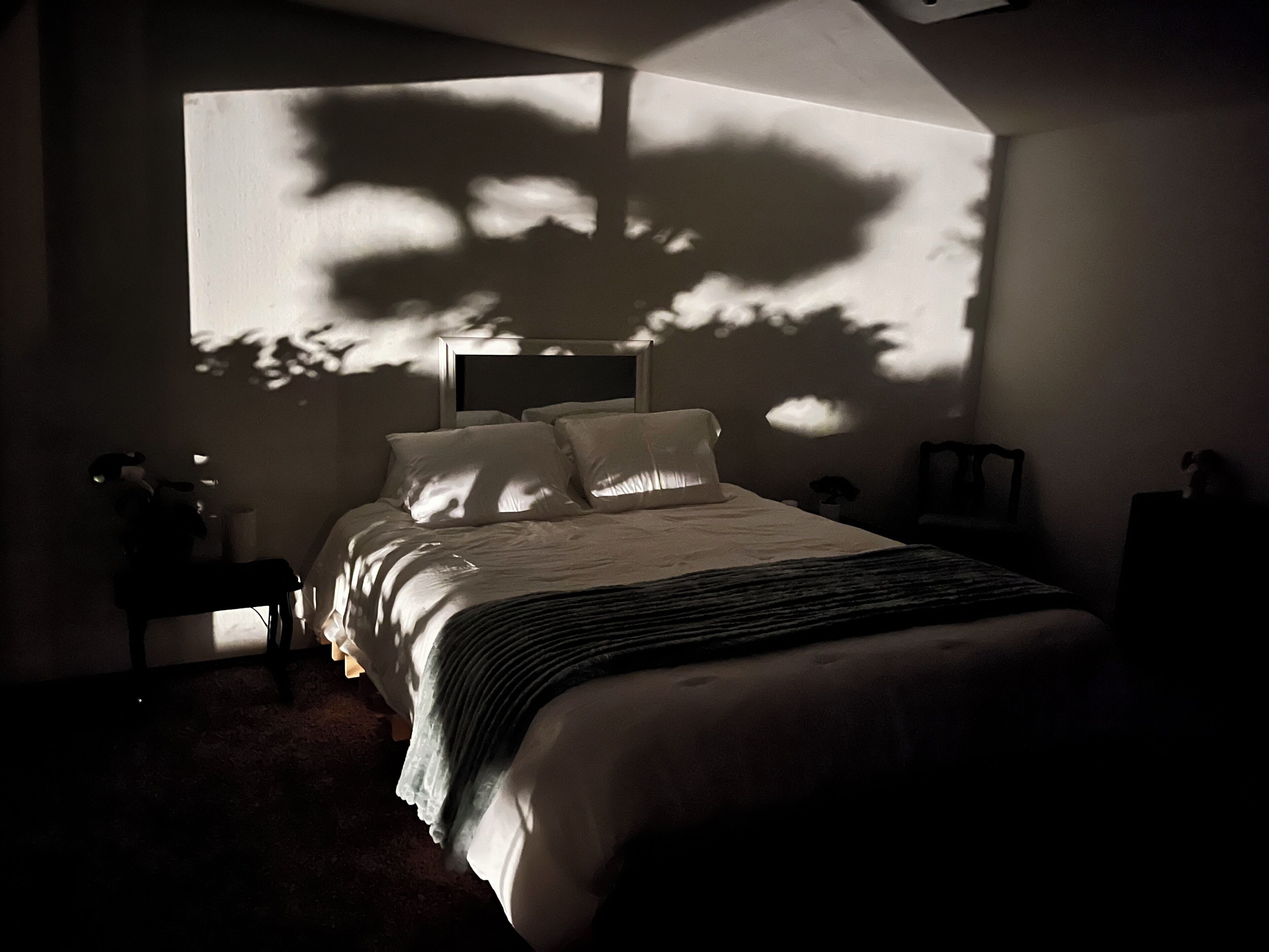 Une chambre à coucher avec un lit, des tables de chevet, une commode et une grande fenêtre qui projette des ombres sur le mur.