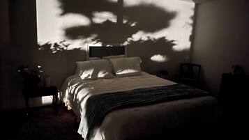 Une chambre à coucher avec un lit, des tables de chevet, une commode et une grande fenêtre qui projette des ombres sur le mur.