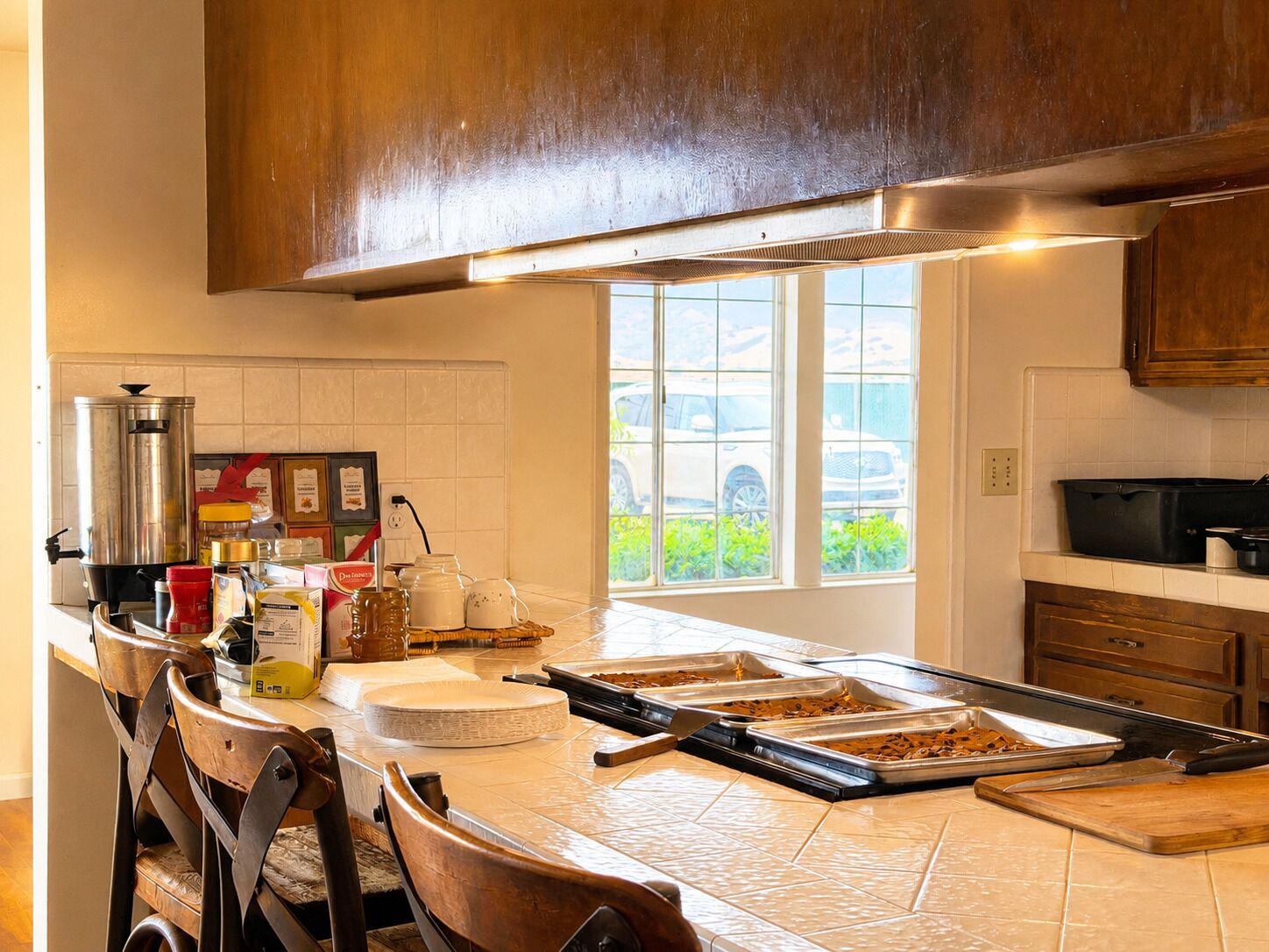 Cozinha ampla com ilha central, cafeteira e janela com vista para carros e vegetação.