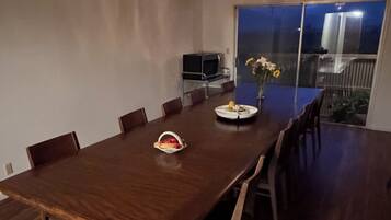 Un coin repas avec une grande table en bois, des chaises, un lustre et un téléviseur posé sur un meuble.