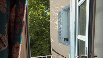An open door to a balcony with a white railing, a blue door with a red handle, and a window with blue shutters.