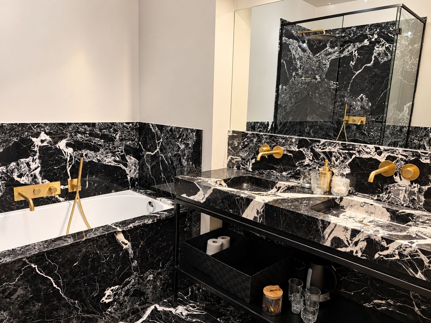 A bathroom with a black and white marble sink, gold fixtures, and a large mirror.