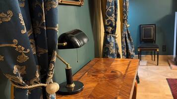 A room with a wooden desk, a lamp, curtains, and a framed picture on the wall.