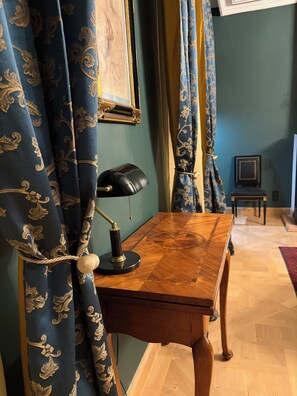 A room with a wooden desk, a lamp, curtains, and a framed picture on the wall.