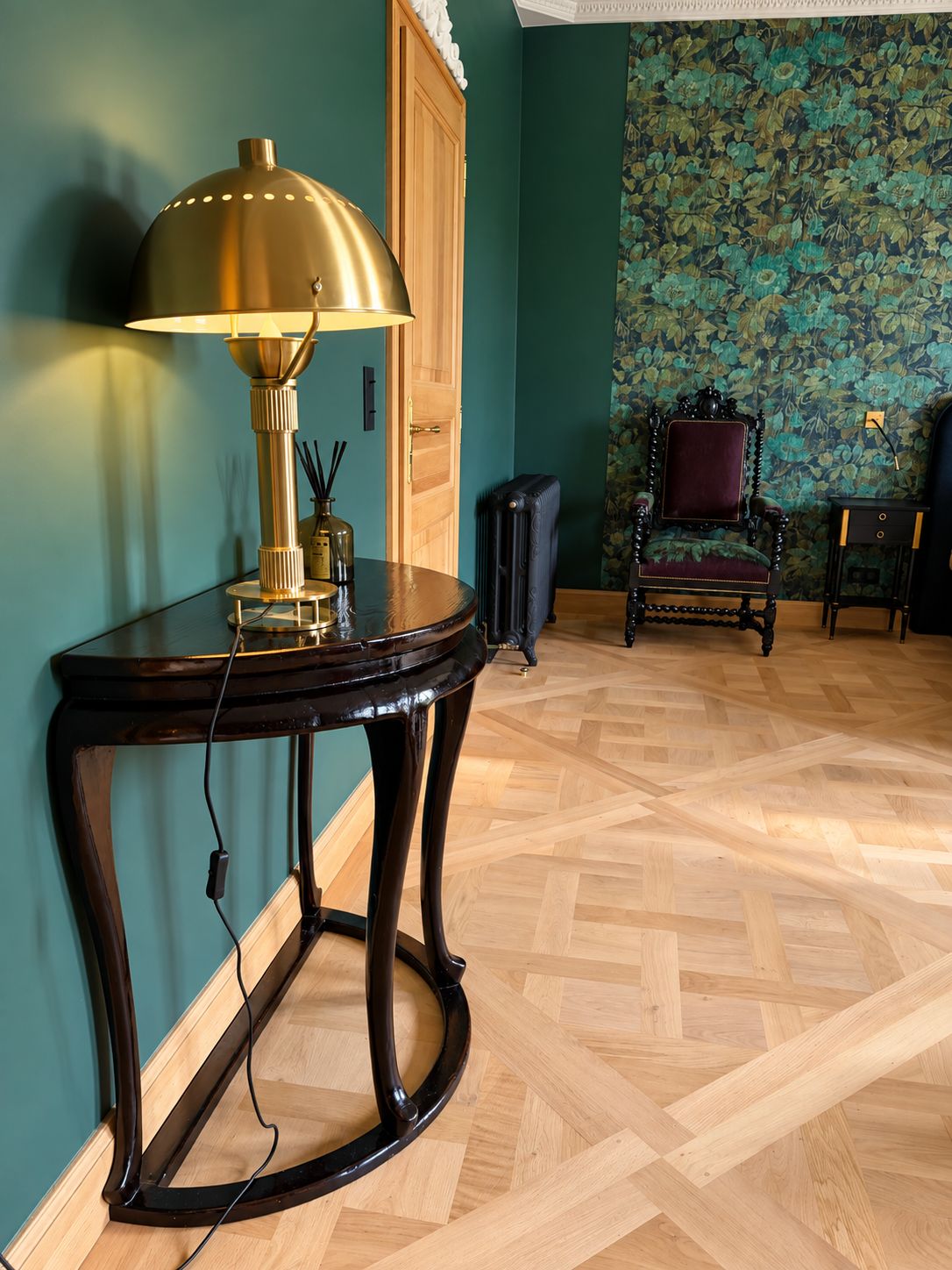 Een kamer met een ronde houten tafel, een lamp, een stoel en behang met een patroon.
