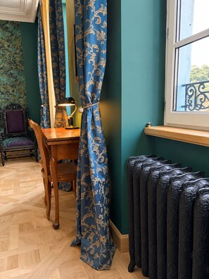 A room with a wooden table, a chair, a lamp, a radiator, and a window with a view. - Maison Crone (Castillon-en-Couserans)