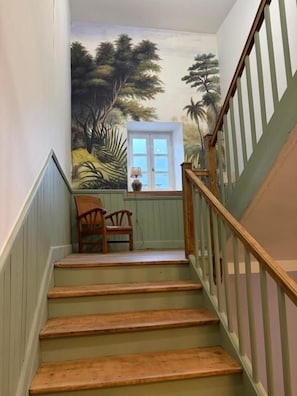 A staircase with wooden steps and a railing, leading to a room with a view of palm trees and a door. - Maison Crone (Castillon-en-Couserans)