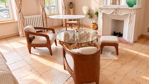A room with a round glass table, wooden chairs, a fireplace, and a view of greenery outside. - Maison Crone (Castillon-en-Couserans)
