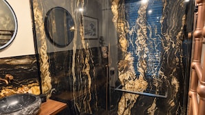 A modern bathroom with a glass-enclosed shower, a wooden vanity with a large basin, and a marble backsplash. - Maison Crone (Castillon-en-Couserans)
