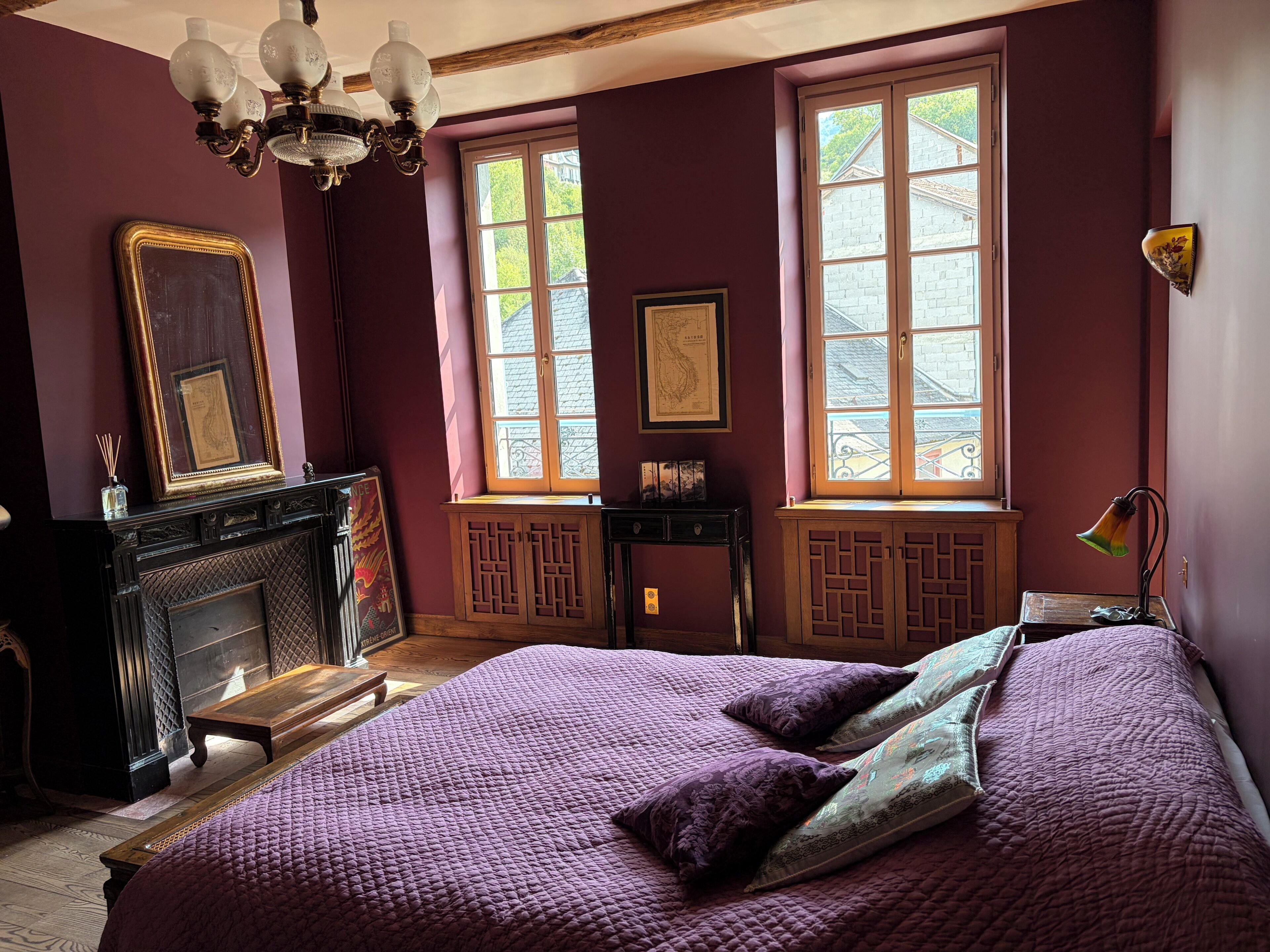 A room with a large bed, a fireplace, and two windows with curtains.